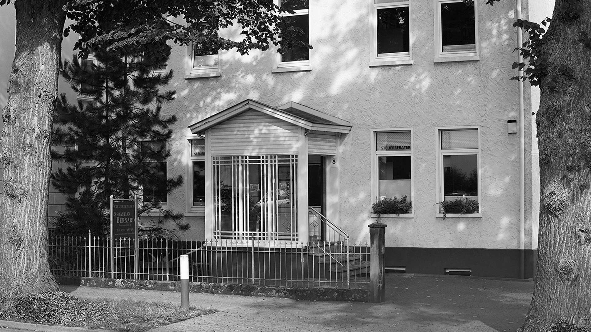 Ruhiges Haus in Hellgrau mit Gittertuer und Baumschatten vorne